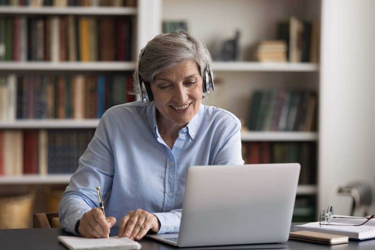 Happy elder student in headphones watching learning webinar on laptop