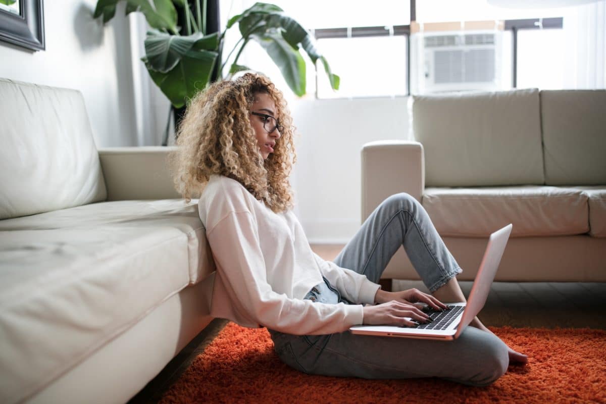 Lady using laptop sat on the floor leaning against a sofa